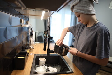 Woman adding ingredients from a pot into a pan while cooking in a clean modern kitchen. Warm and natural lifestyle scene