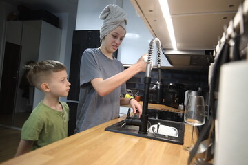 Woman helping a young boy wash hands at the kitchen sink, sharing a warm family moment in a modern home