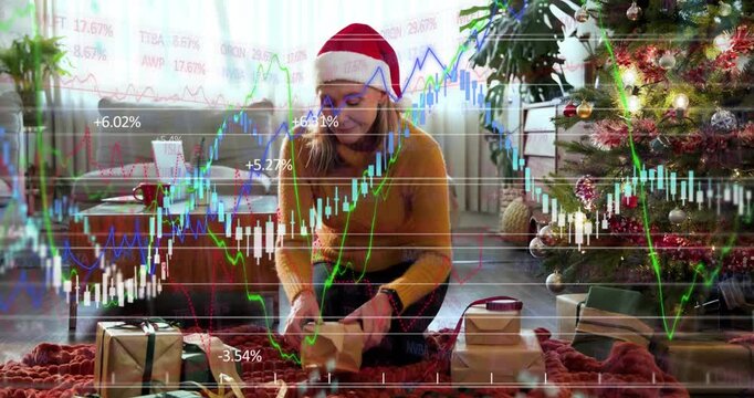 Woman kneeling reaching for box, wrapping gifts for holiday while finance charts moving over hands