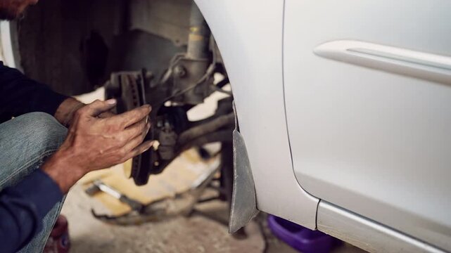 Detailed closeup of mechanic's hands fixing suspension and brake system under the car in auto garage.