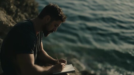 Man writing on notebook sitting on the rocks by sea, lifestyle concept