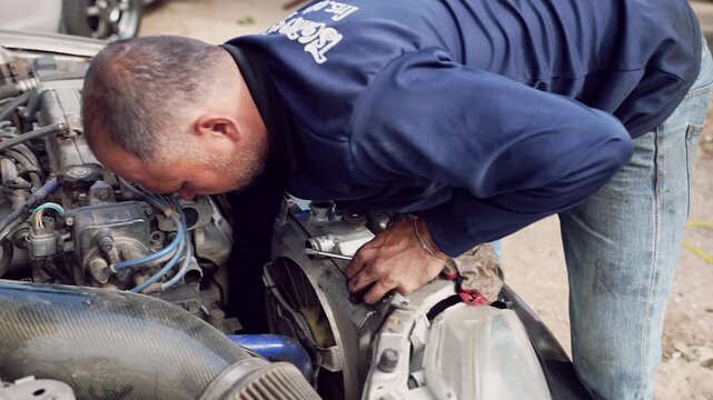 Skilled technician working on open engine bay with tools and dirty hands, focused repair action.