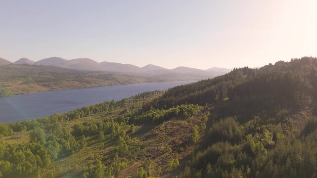 evening light over Loch Garry in Scotland flying over trees and logging operations looking west over the water of the loch