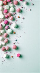 Fototapeta premium A top-down view of various round candies and sprinkles in pastel pink, white, and orange hues scattered across a light blue, textured surface. The candies are a
