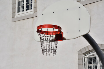 Basketball net with red ring and chain on a white wall background.