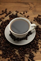 Aromatic coffee in cup and beans on wooden table, closeup