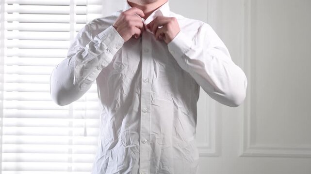 Man putting on creased shirt indoors, closeup
