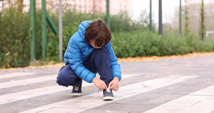 Little boy tying shoelaces on pedestrian crossing outdoors. Child in danger and road safety