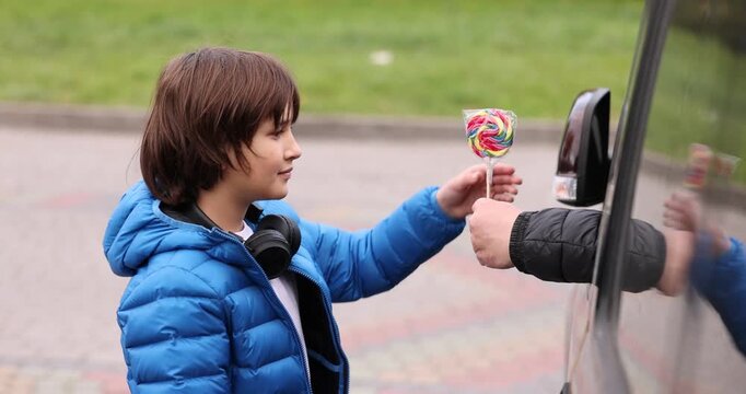 Stranger in car giving lollipop to little boy outdoors, closeup. Child in danger