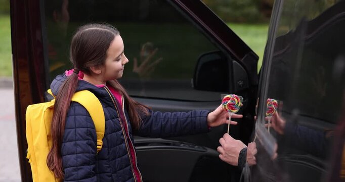 Stranger in car giving lollipop to little girl outdoors, closeup. Child in danger