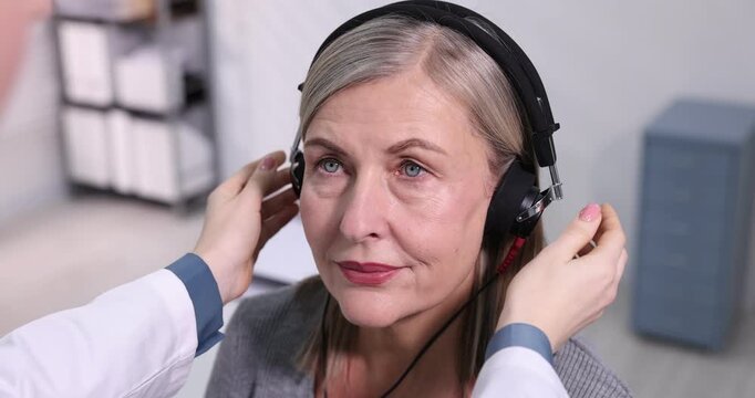 Hearing test. Doctor adjusting patient's audiometric headphones in clinic, closeup. Camera moving
