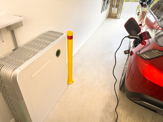 Electric car EV plugged in on charge in a garage with active solar battery wall installation green light showing solar storage