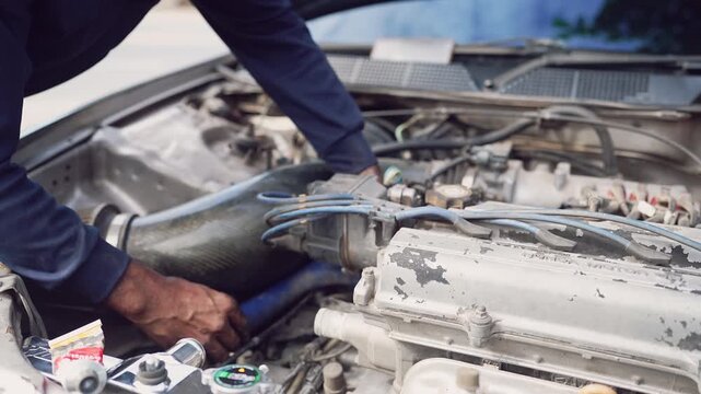 Close-up of mechanic using silicone sealant while working on engine system under the hood.