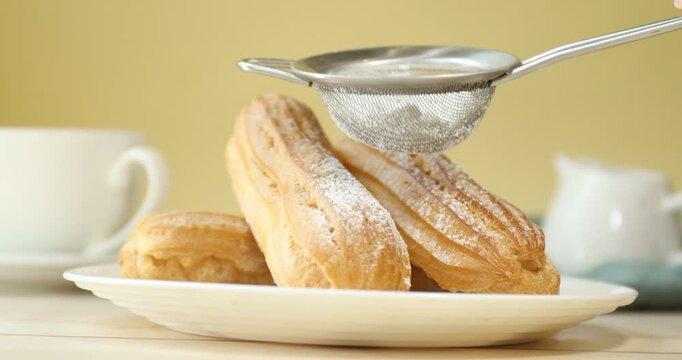 Woman sprinkling eclairs with powdered sugar at white wooden table, closeup