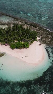 Island with dense palm trees, white sandy beach, anchored boats and turquoise shallow water. Guyam Island. Siargao, Philippines.