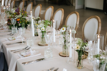 Rustic Elegant Wedding Table Setting with Wildflowers, Tall Candles, and Crystal Glasses in Bright Venue