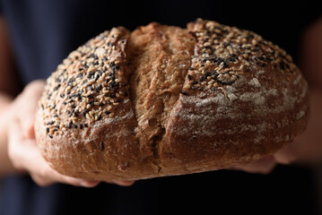 Dark rye sourdough bread topped with sesame seeds, a healthy vegetarian food, held in a woman's hand.
