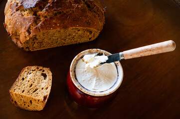 A slice of sourdough bread next to a pot of butter with a knife in it