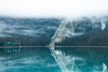 Serene lake view reflecting the forest and fog-covered mountains above.