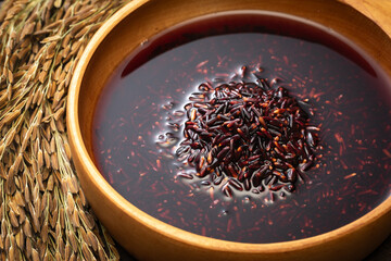 Black rice and rice water are in a wooden bowl. Rice ears are placed beside it.