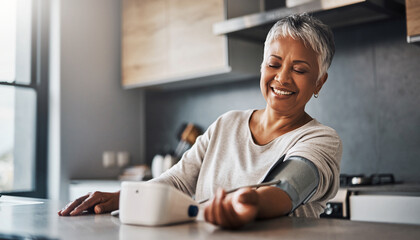 Happy senior woman using smart blood pressure monitor at home, smiling and relaxed in modern kitchen, healthy lifestyle, independent living, wellness, technology for elderly
