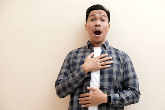 Southeast Asian man wearing flannel shirt showing shocked face expression, on white isolated background.