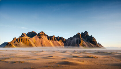 A serene and majestic mountain range in Iceland emerging from a blanket of morning fog over a vast golden sand beach landscape