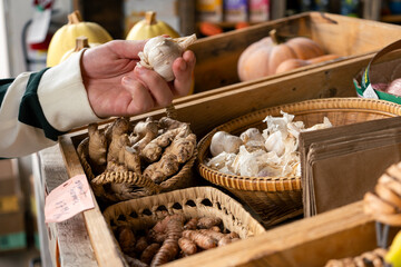 Hand picks garlic at the farm stand, surrounded by fresh produce display.