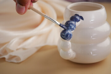 Painting decorative design on ceramic pot in home studio