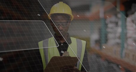 Standing warehouse tech wearing yellow hardhat hi-vis vest holding clipboard, checking with grid UI