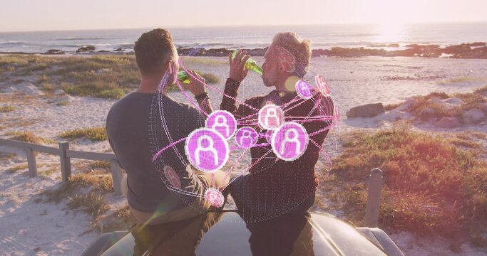 Sitting men in sweaters drinking green bottles on car roof at beach sunset, with pink overlay - Powered by Adobe