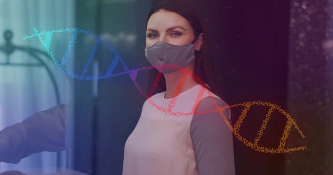 Standing mid-adult woman wearing grey cloth face mask in clinic, multicolored DNA helix overlay - Powered by Adobe