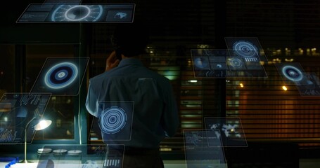 Talking man in blue shirt, dark pants using smartphone at dim office, monitoring holographic UI