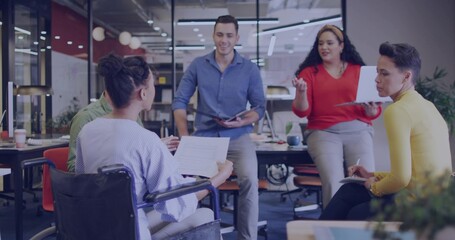 Discussing, four team members in open office reviewing papers, wheelchair, laptop, red top