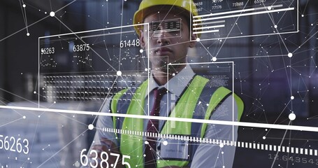 Checking site engineer viewing digital UI inside warehouse, yellow hard hat, lime vest, ID badge