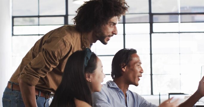 Leaning Mid Adult man and colleagues wearing casual shirts gesturing at monitor in bright office
