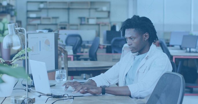 Working man with dreads typing on laptop in office, wearing light shirt, watch, with monitor charts - Powered by Adobe