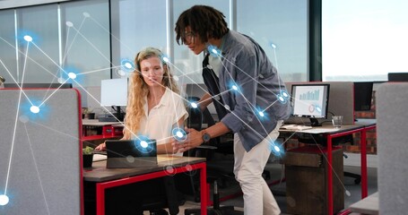 Leaning man pointing at tablet in office, seated woman typing at red desk, network overlay, charts