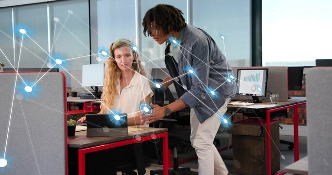 Leaning man pointing at tablet in office, seated woman typing at red desk, network overlay, charts - Powered by Adobe