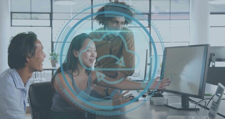 Pointing woman in sleeveless top typing with team at desk, showing monitor and cloud-sync overlay