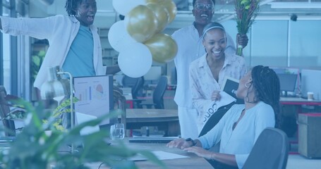 Presenting team celebrating seated coworker in casual business attire at office with balloons