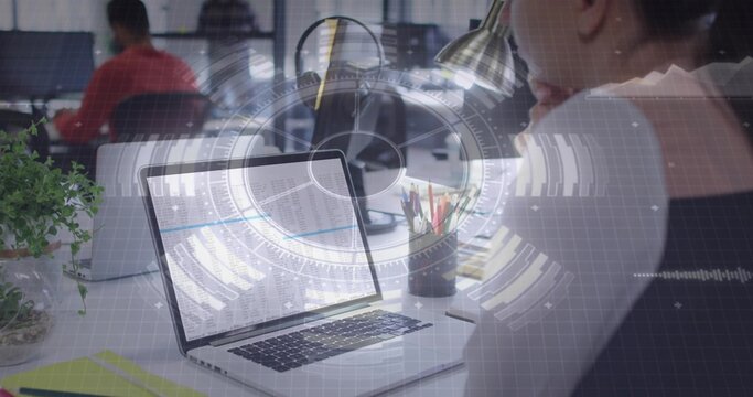 Displaying silver laptop showing spreadsheet at office desk, with woman in dark top, HUD overlay