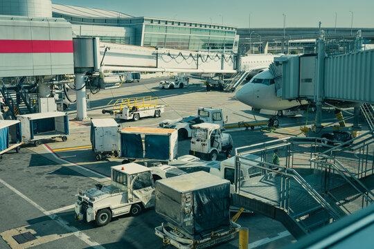 Busy airport tarmac with cargo handling vehicles and passenger boarding bridge.
