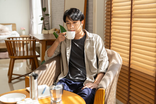 Man lifestyle enjoying coffee at home in cozy chair with sunlight through blinds