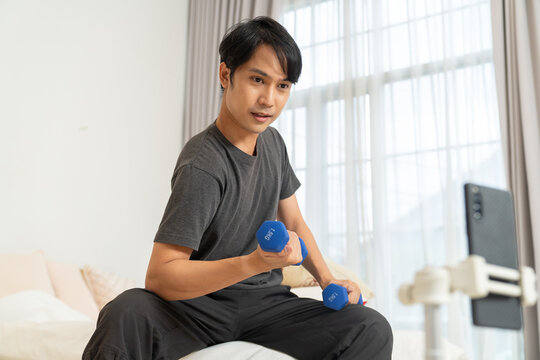 Man lifestyle exercising with dumbbell home recording video for social media fitness content