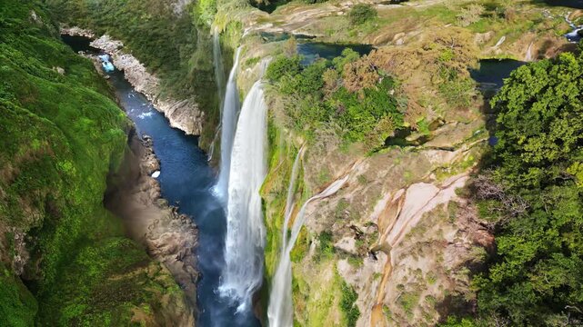 Aerial drone view of Tamul Waterfall cascading down green cliffs into a turquoise pool below