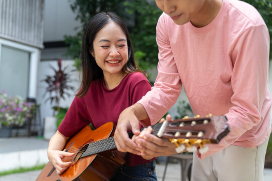 Young woman smiling while learning to play acoustic guitar with man outdoors
