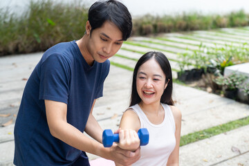 Young woman exercising with dumbbell and male trainer helping outdoors smiling