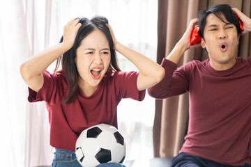 Couple watching soccer game with intense emotions holding ice packs on head indoors
