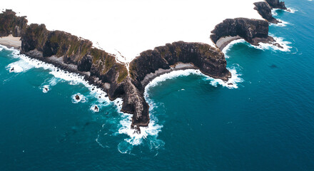 Dynamic aerial view reveals majestic coastal cliffs meeting the vast blue ocean as powerful foamy waves intensely crash ashore.. AI Generated